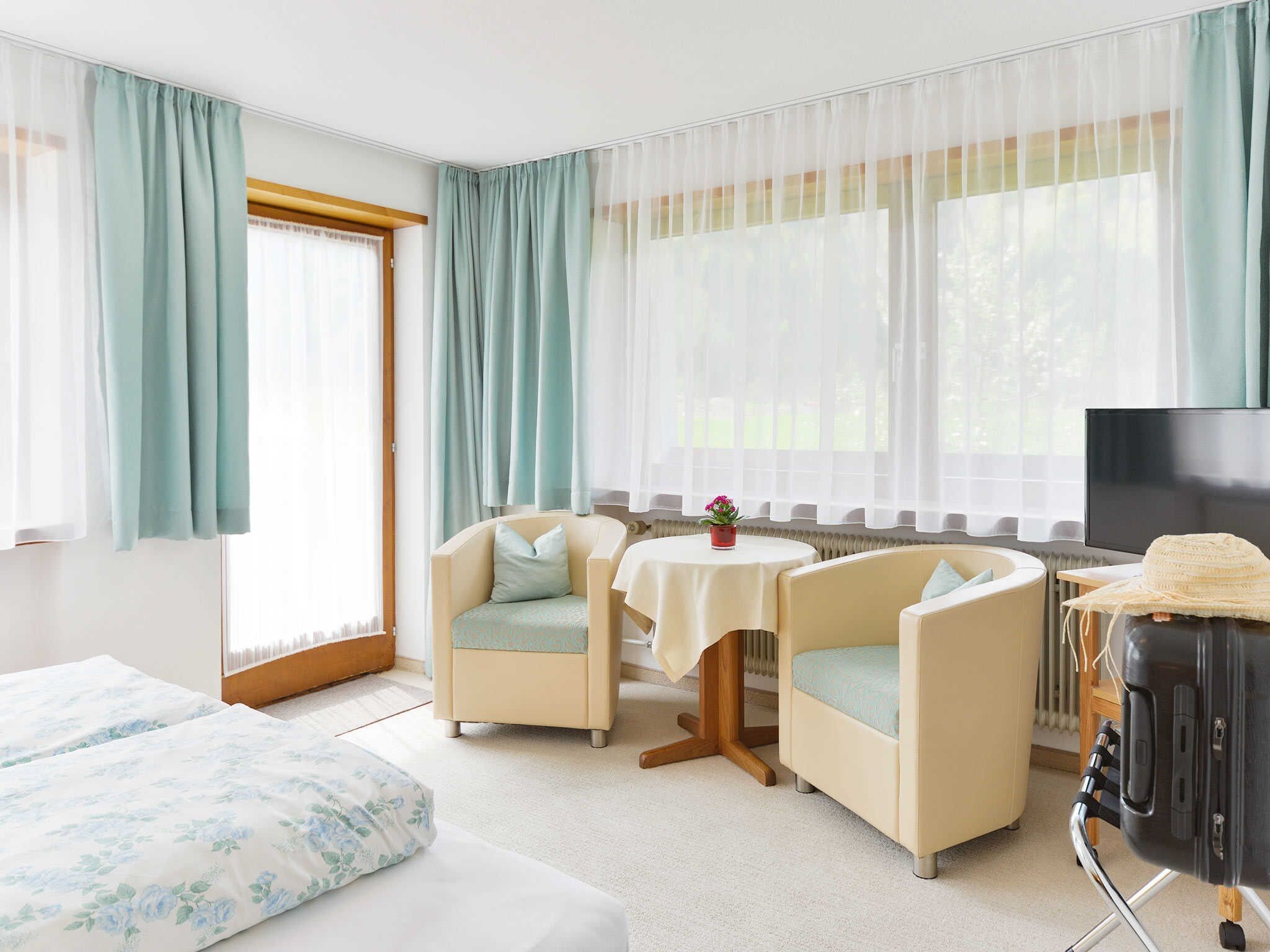 Camera d'albergo con due poltrone, un tavolino, una televisione e un letto.