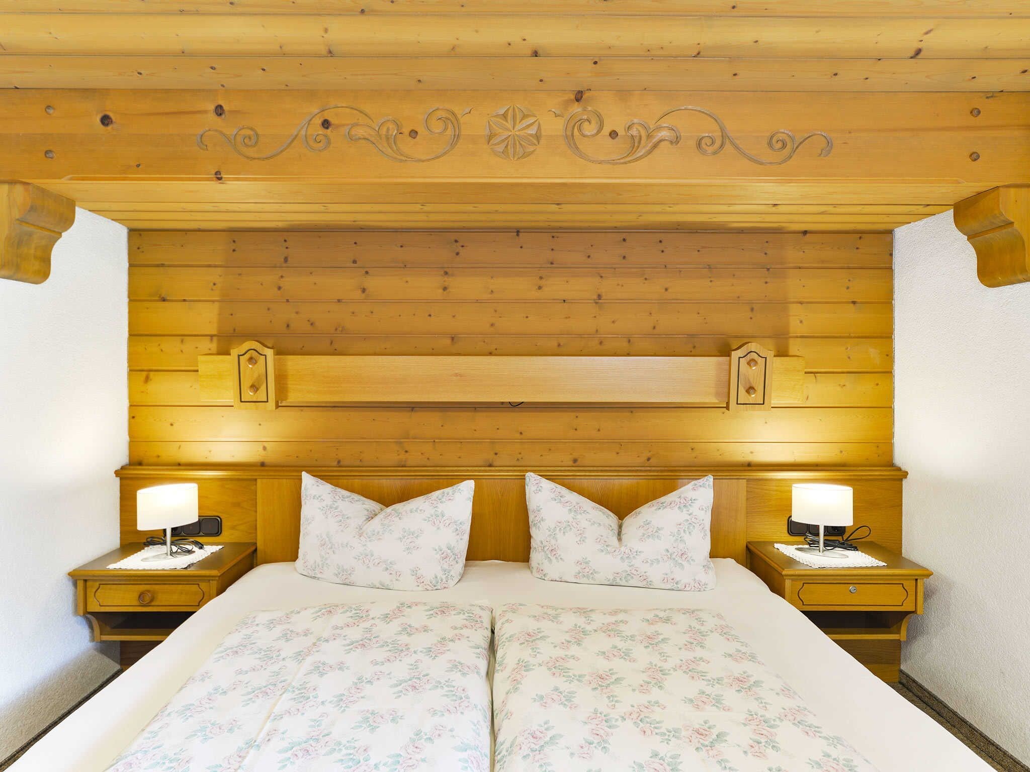A wooden-paneled bedroom with a large bed, two bedside tables, and decorative wall carvings.