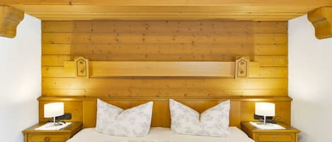 A wooden-paneled bedroom with a large bed, two bedside tables, and decorative wall carvings.