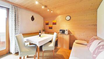 A cozy room with a dining table, chairs, a microwave, a sofa, and a clock on the wall.