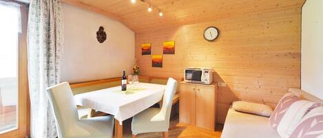 A cozy room with a dining table, chairs, a microwave, a sofa, and a clock on the wall.