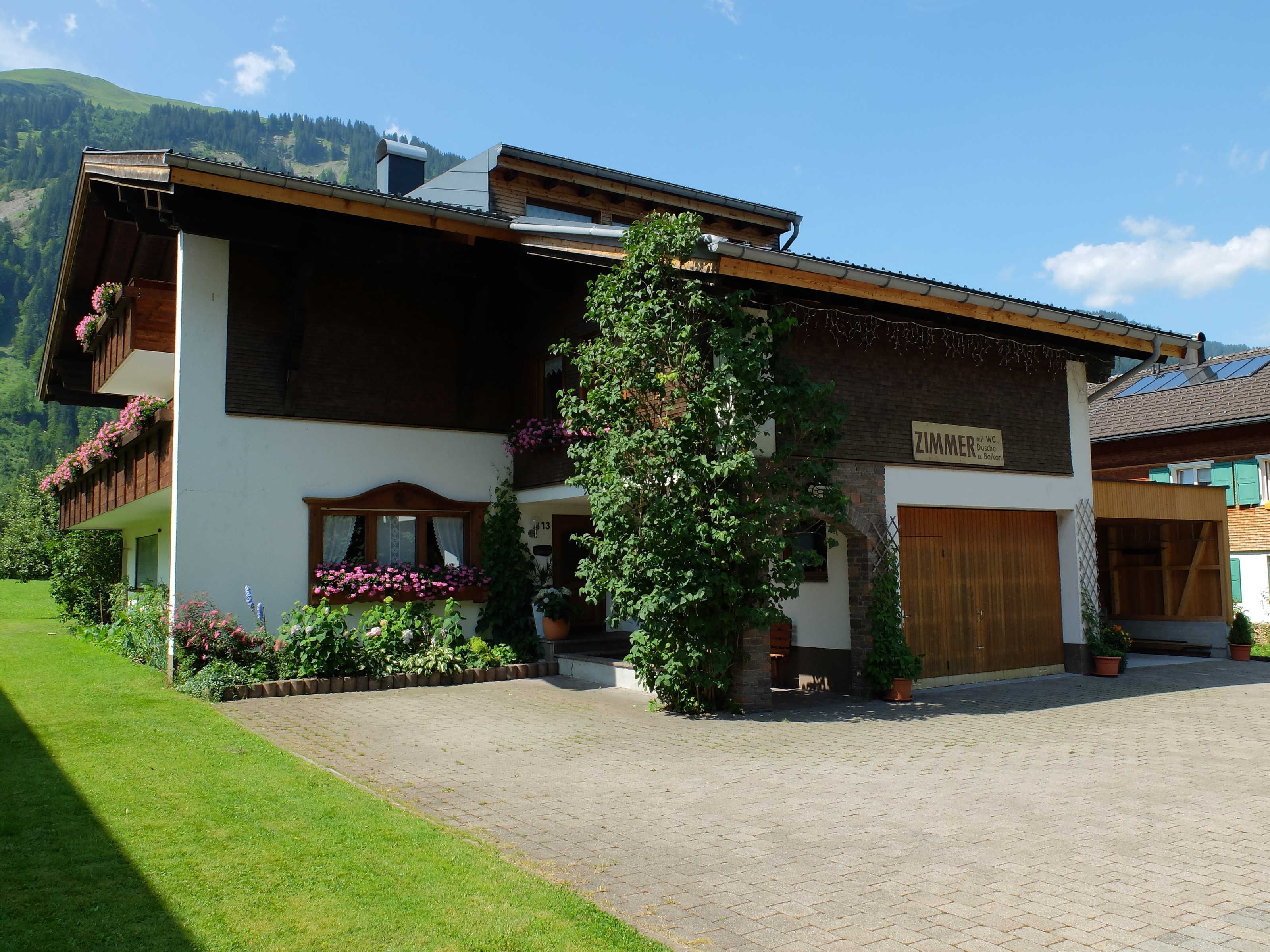 Un bâtiment à deux étages avec une façade en bois, une enseigne indiquant « ZIMMER » et une allée pavée.