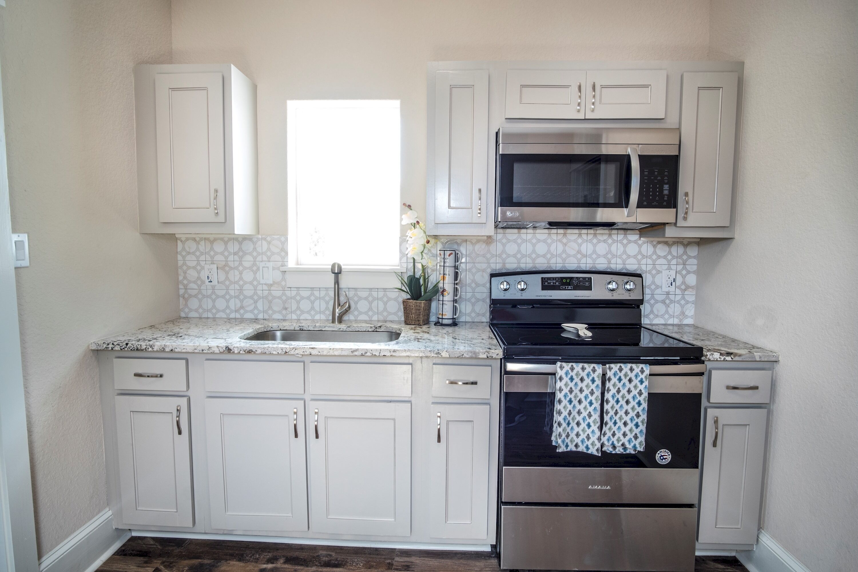 A kitchen with white cabinets, a stainless steel oven, a microwave, and a sink.