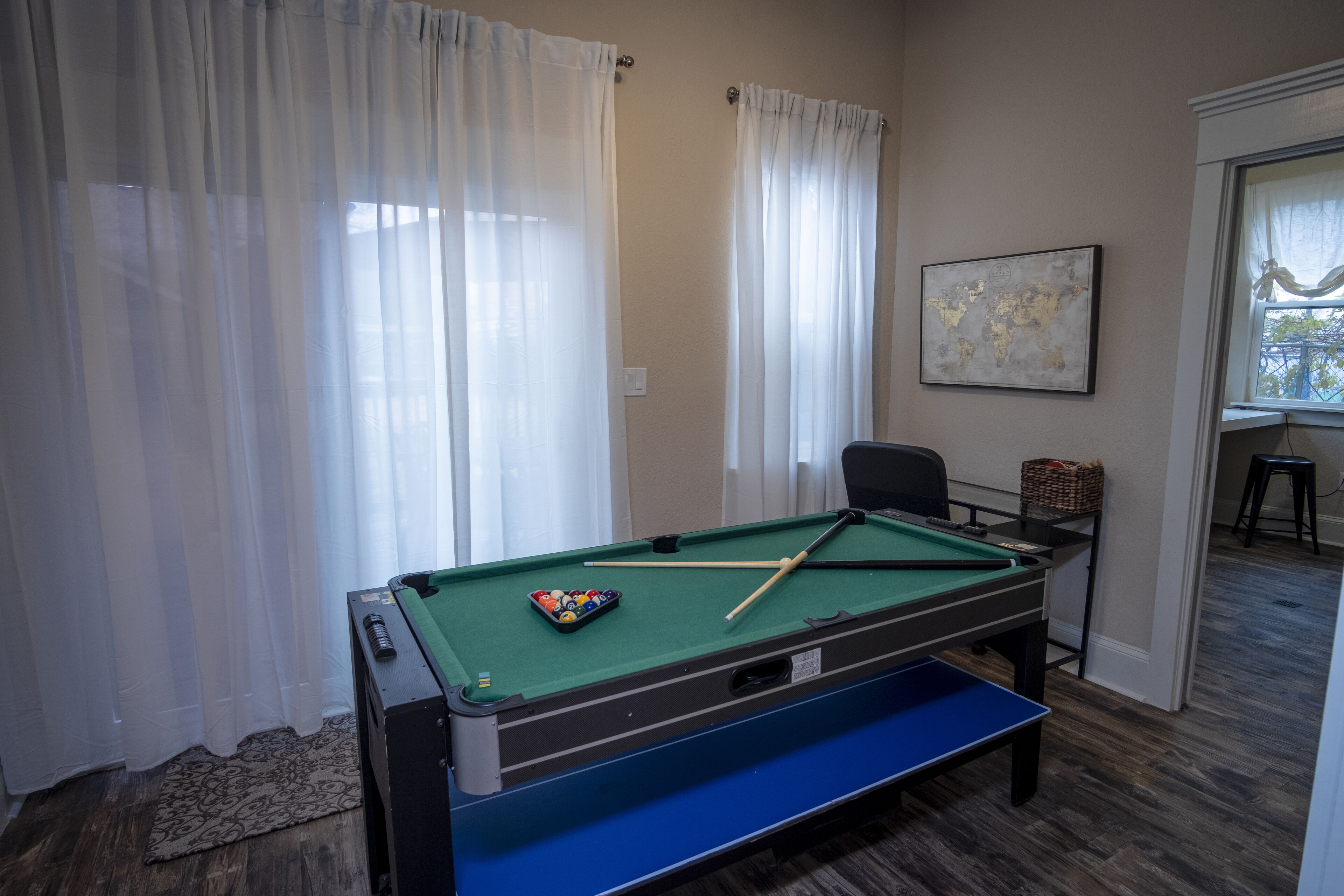A pool table in a room with a window, curtains, and a map on the wall.