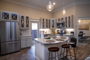 A modern kitchen with stainless steel appliances, white cabinetry, and a central island with stools. - Brand NEW Large Impressive House Near Downtown! (San Antonio)