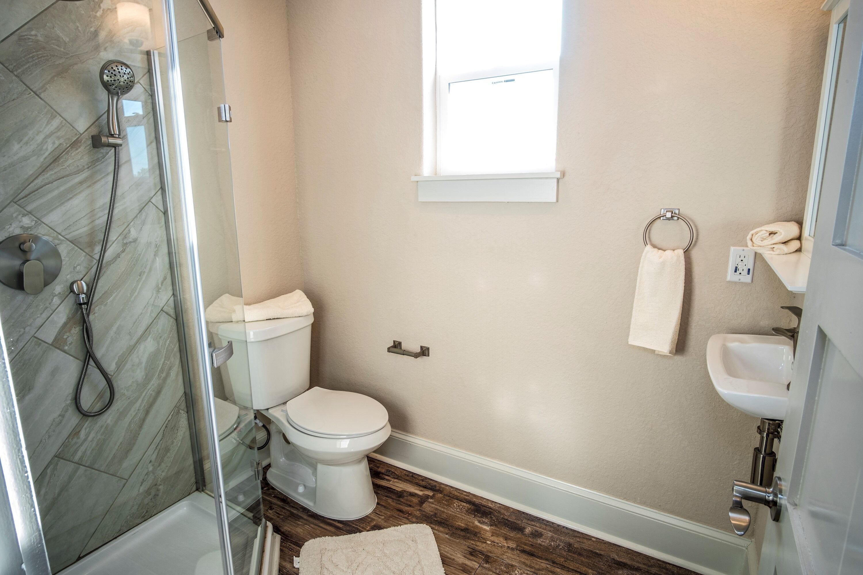 Une salle de bain avec une douche à parois de verre, des toilettes, un lavabo et une fenêtre.