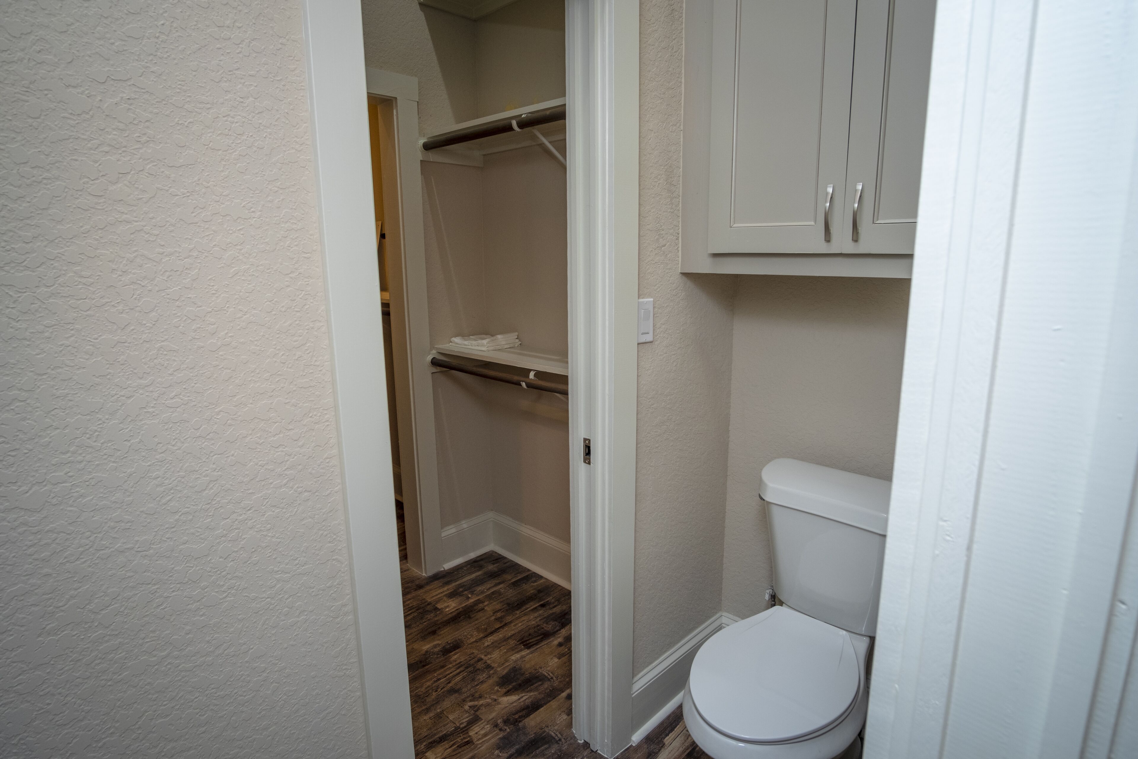 A small bathroom with a white toilet, a wooden floor, and a white shower curtain.