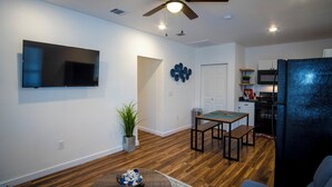 A modern living room with a flat-screen TV, wooden flooring, a ceiling fan, and a dining area with a table and chairs. - Downtown View Cozy 2br/1ba Home Sleeps 8 (San Antonio)