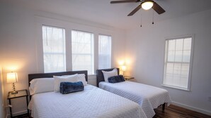 A hotel room with two beds, a ceiling fan, and large windows with blinds. - Downtown View Cozy 2br/1ba Home Sleeps 8 (San Antonio)