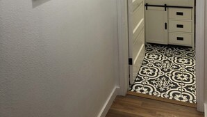 A hallway with a white wall, black-framed mirrors, a white door leading to a bathroom, and a patterned floor. - Downtown View Cozy 2br/1ba Home Sleeps 8 (San Antonio)