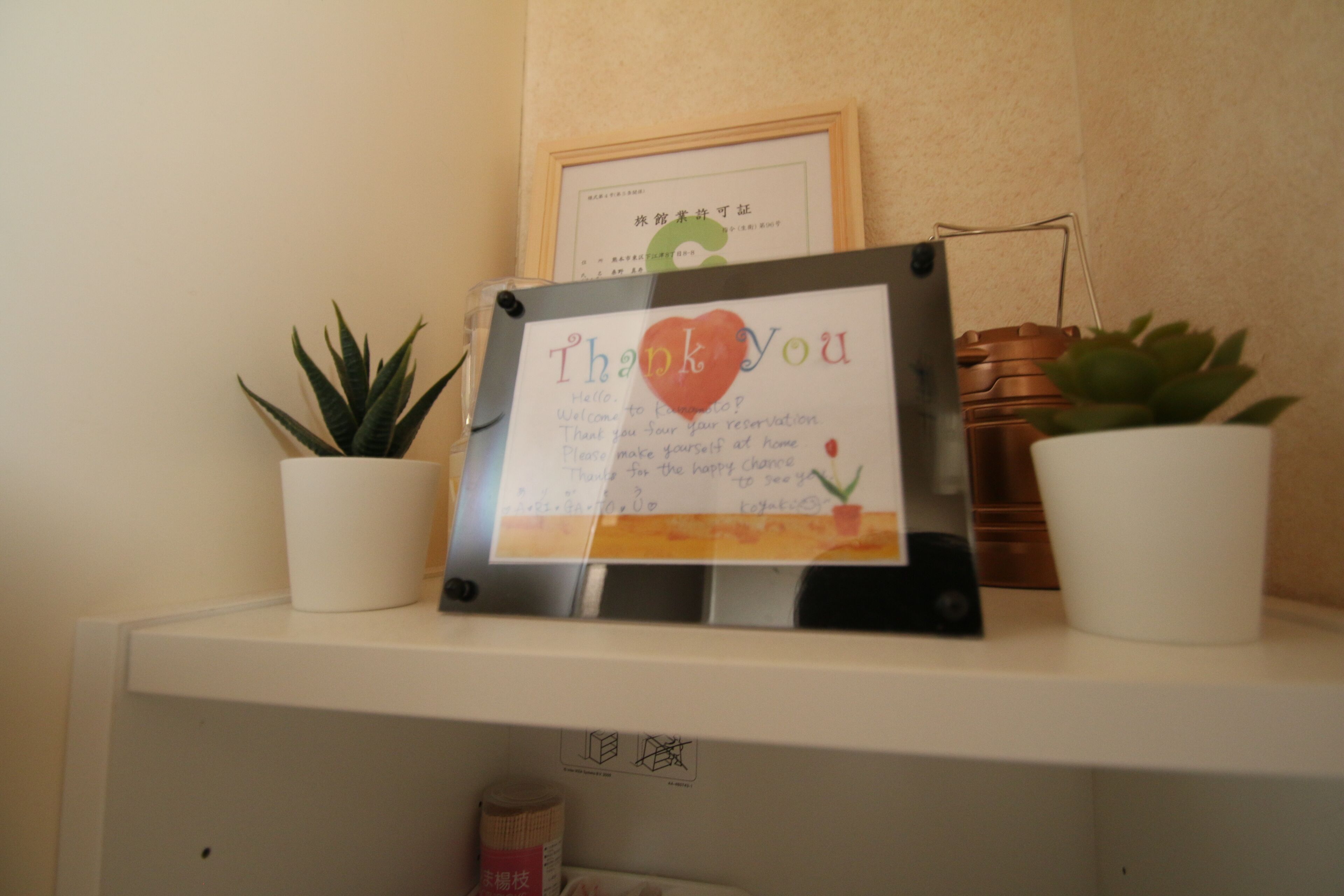 Cartell amb la frase 'Thank You' i un cor, emmarcat, sobre una estant blanca amb plantes en testos.