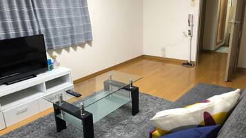 Un salon équipé d’un téléviseur à écran plat, d’une table basse en verre, d’un canapé et d’un tapis gris.