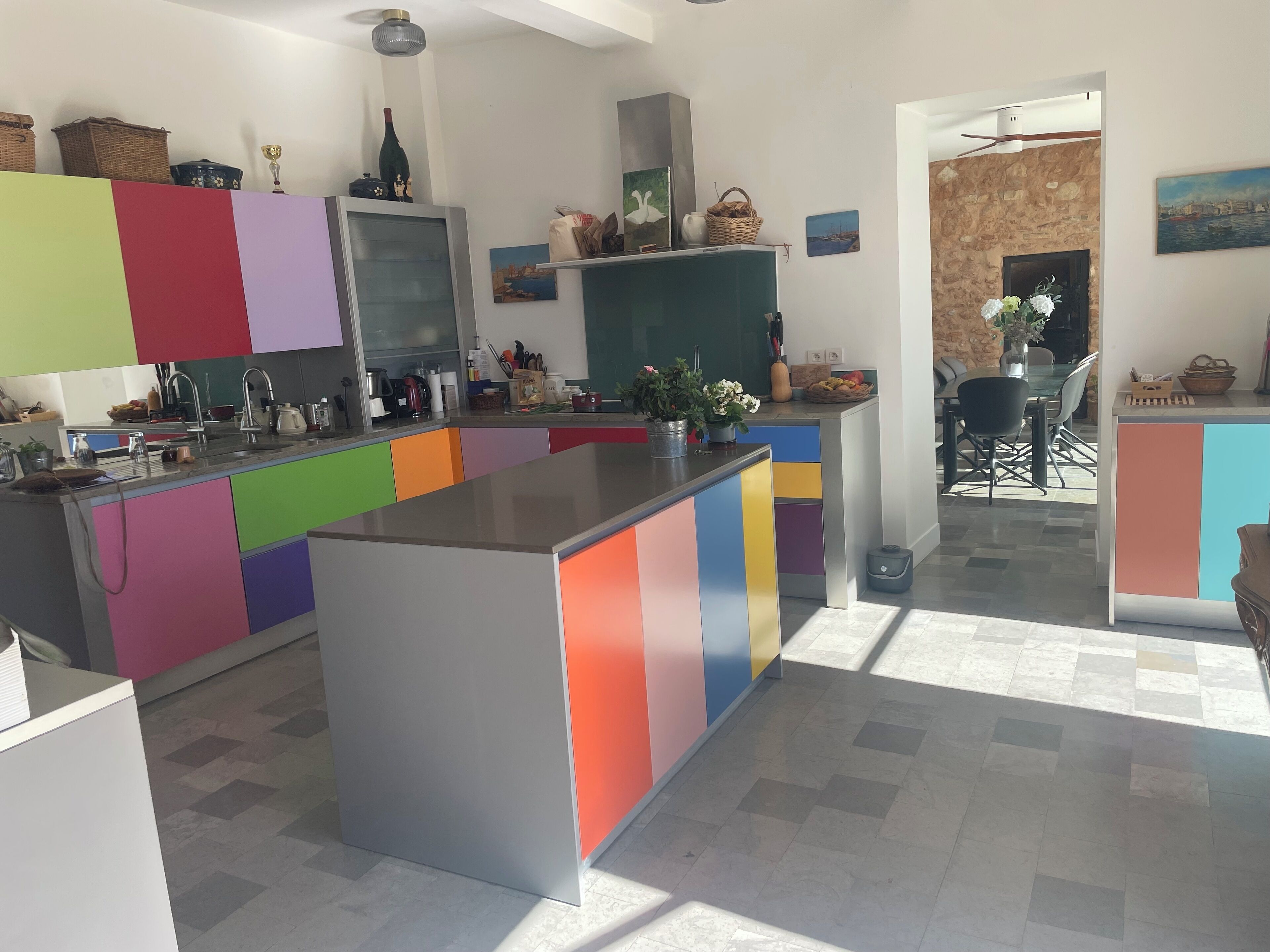 A modern kitchen with colorful cabinets, a central island, and a dining area with a stone wall and a view.