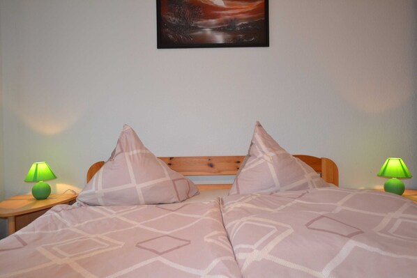 A bedroom with a wooden headboard, two green lamps on nightstands, a painting above the bed, and a patterned bedspread. - Wendt apartment, Germany (Insel Poel)