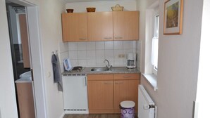 A compact kitchen with wooden cabinets, a sink, a coffee maker, and a small trash bin. - Wendt apartment, Germany (Insel Poel)