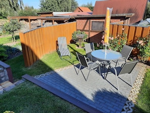 A patio with a round table and chairs, a striped lounge chair, and a wooden fence.