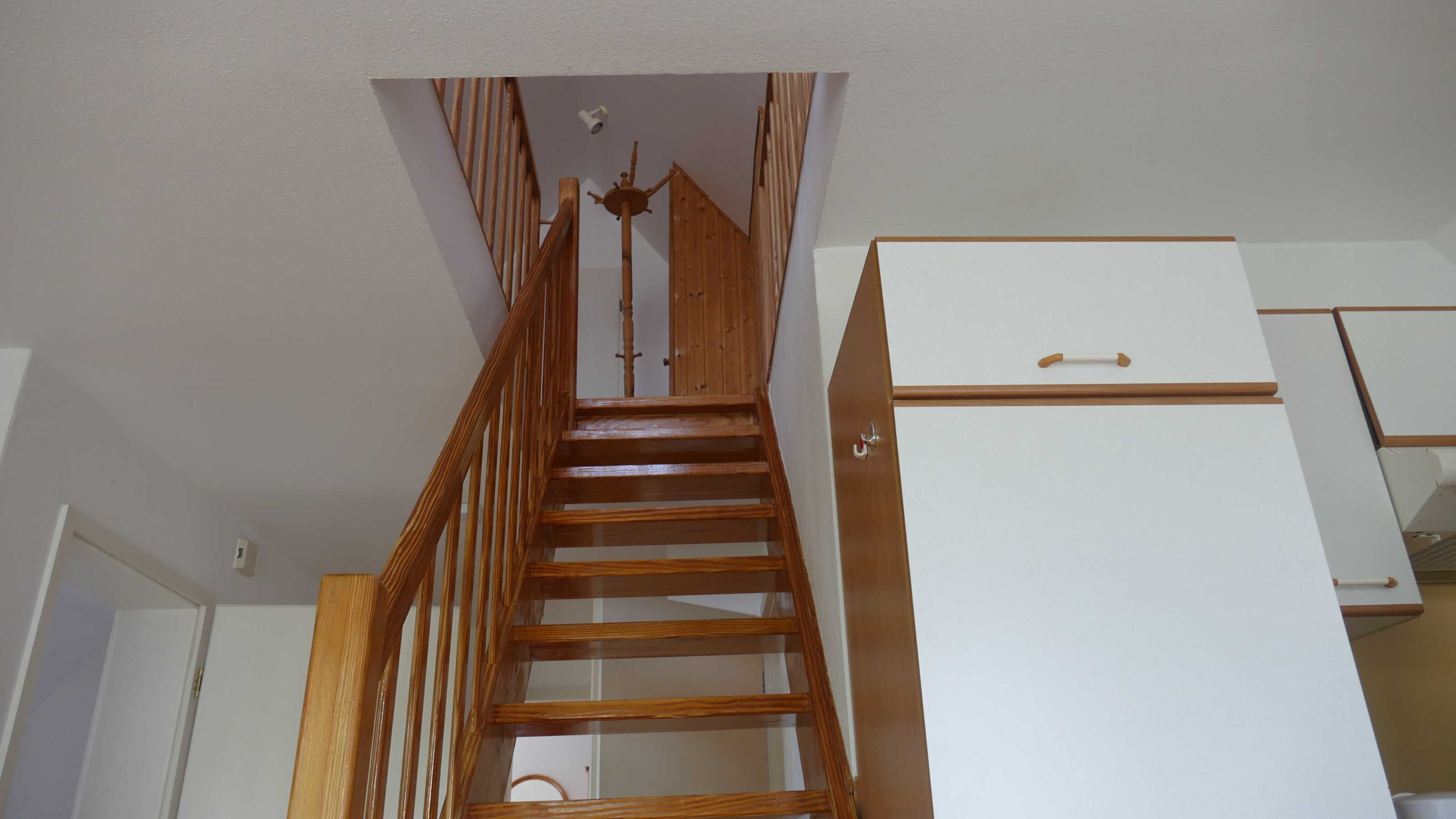 Un escalier en bois menant à un palier où se trouvent un meuble blanc et une porte.