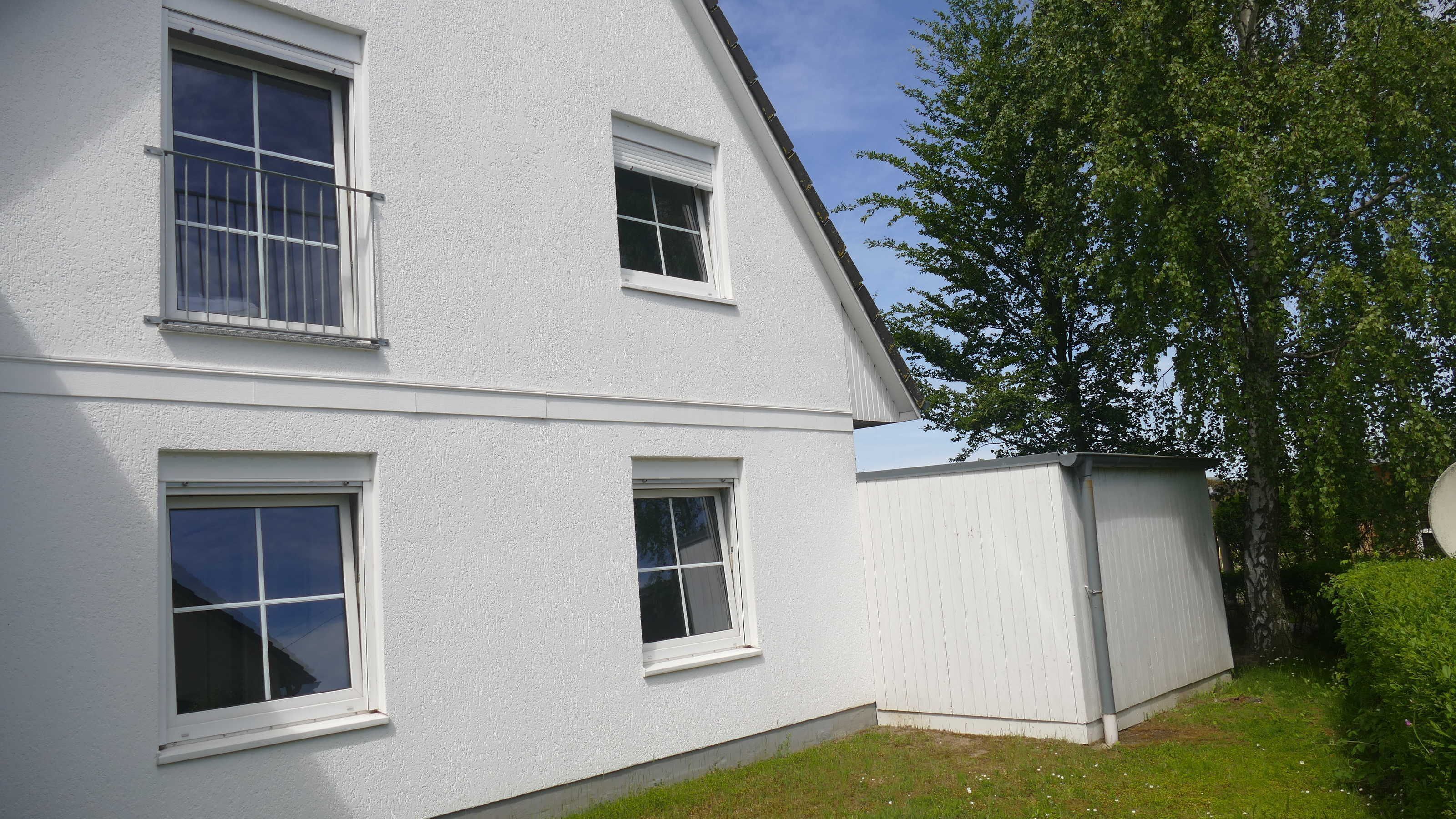 A white two-story house with three windows and a small attached garage.