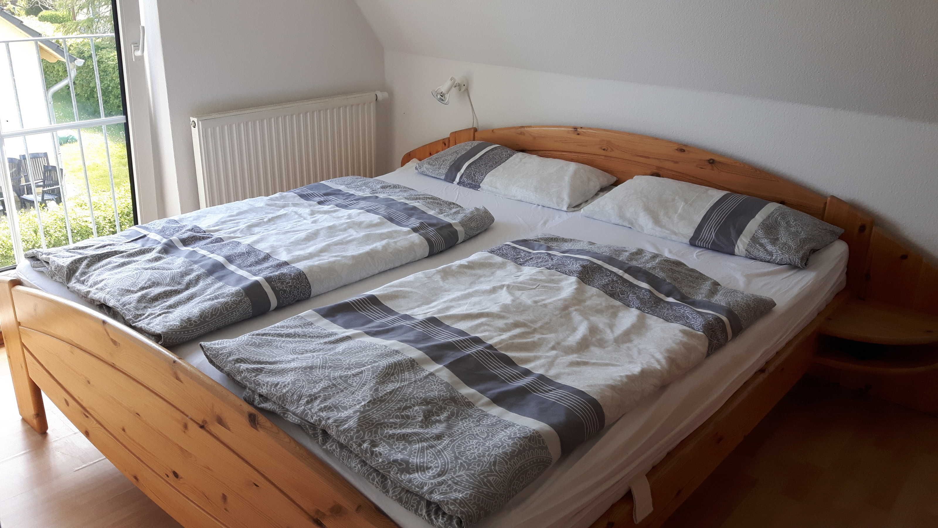 Uma cama de madeira com colchão branco e mantas cinzas com padrão.