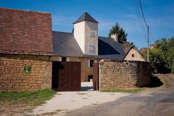 Un edificio de piedra tradicional con una torre central, un camino de grava y un cartel que indica una casa rural.