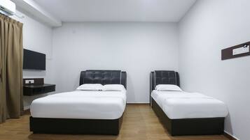 A hotel room with two single beds, a small bedside table, a flat-screen TV mounted on the wall, and a window with curtains.