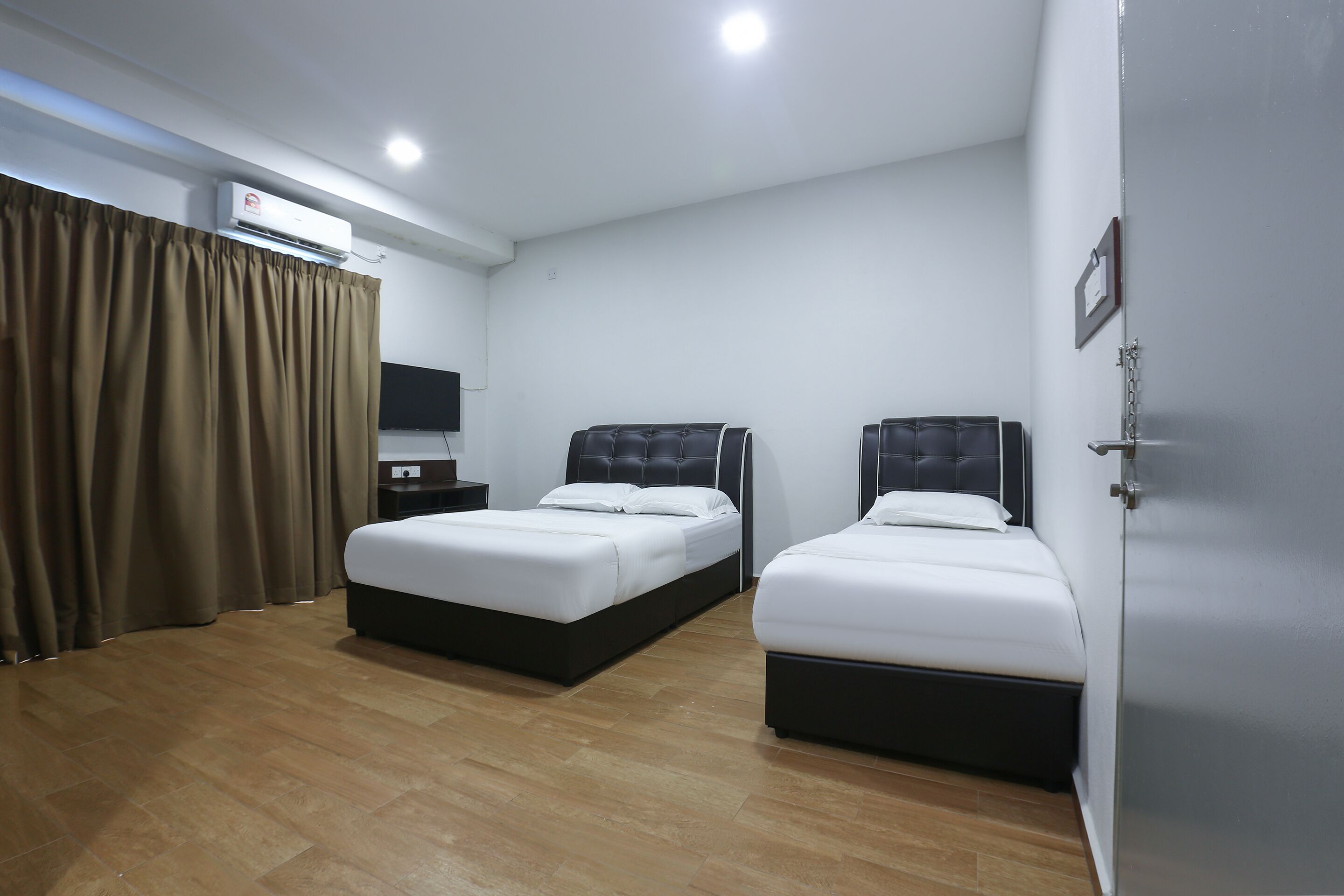 A hotel room with two beds, a flat-screen TV, an air conditioning unit, and a wooden floor.