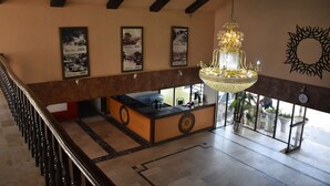 A lobby with a reception desk, a chandelier, and framed historical photos on the wall. - Grand Heights Hotel (Murree)