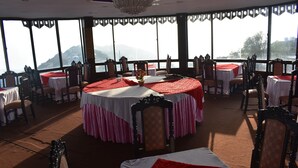 A dining area with round tables, chairs, and a chandelier. - Grand Heights Hotel (Murree)
