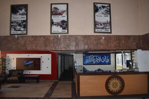 A lobby with framed historical photos, a TV, a reception desk with Arabic script, and a staircase leading to another area. - Grand Heights Hotel (Murree)