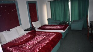 A hotel room with two beds, green curtains, and a small table. - Grand Heights Hotel (Murree)
