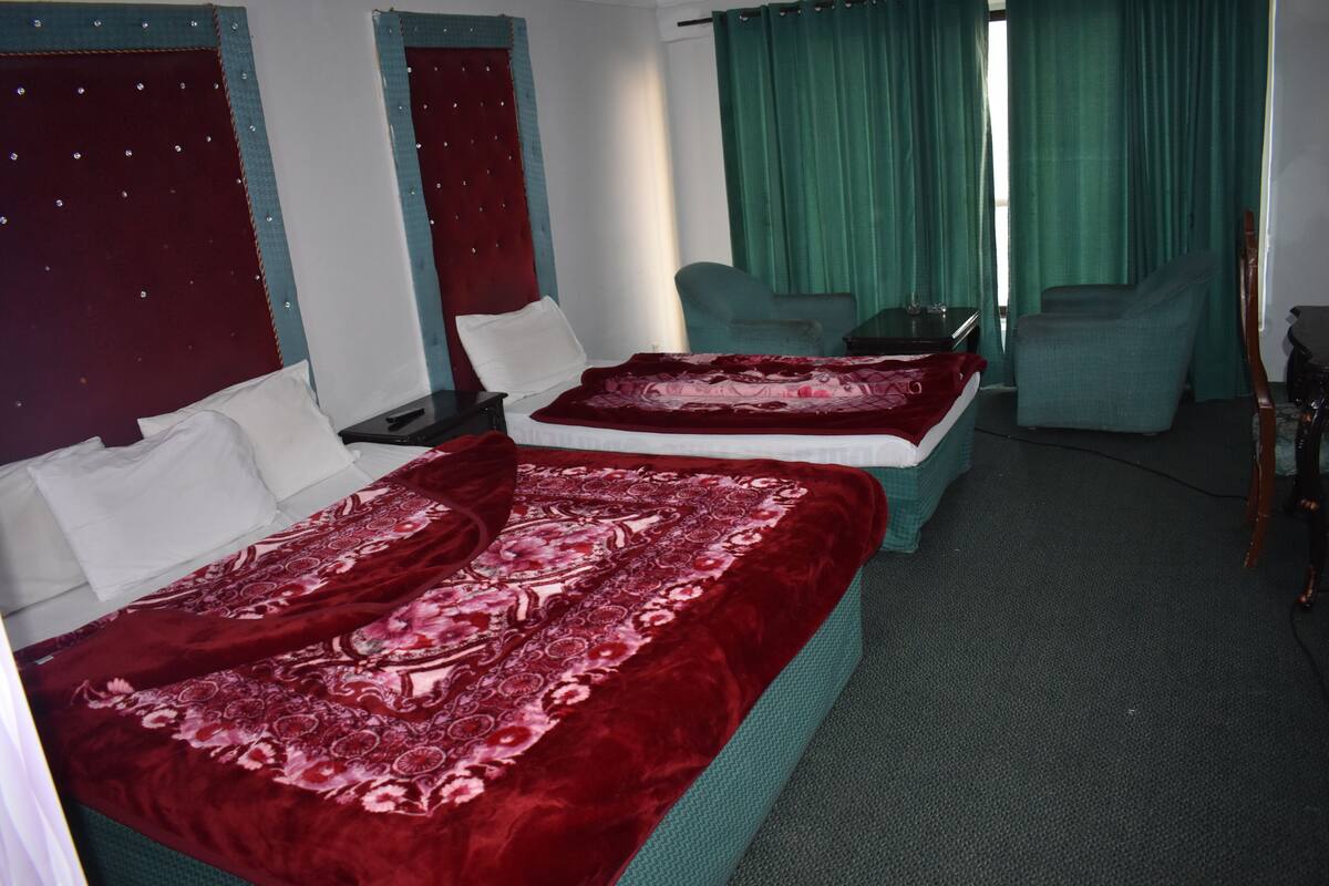 A hotel room with two beds, green curtains, and a small table.