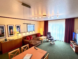 Ein Hotelzimmer mit einer braunen Ledersofa, einem Holzesstisch, einem Fernseher und gerahmten Bildern an der Wand.