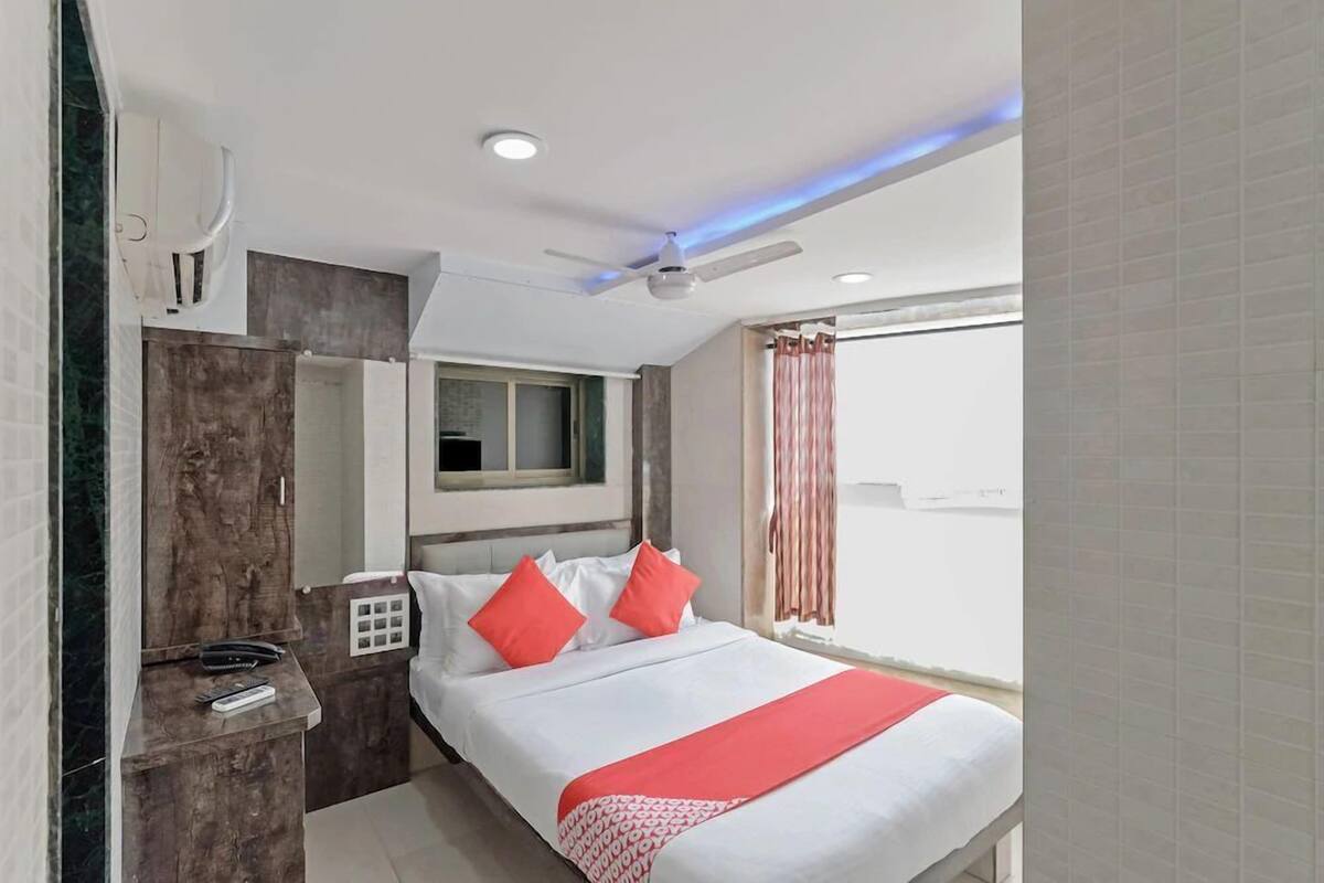 A hotel room with a bed, a desk, a wardrobe, a ceiling fan, and a window with curtains.