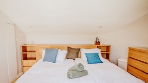 A neatly made bed with white linens and a pair of rolled towels. There are wooden headboards and a small shelf with a bottle and remote controls. - Luxury Triplex In Jerusalem Center (Jerusalem)