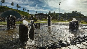 Et vandelement med flere vandstråler, omgivet af sten og en belagt flade.