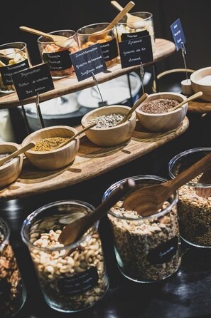 A variety of food items displayed in wooden bowls and jars, each labeled with their name. - Waer Waters spa Hotel (Dilbeek)