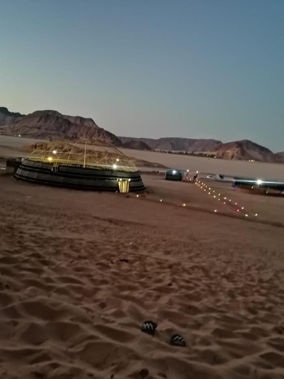 A desert landscape with a large, illuminated structure resembling a tent or pavilion.