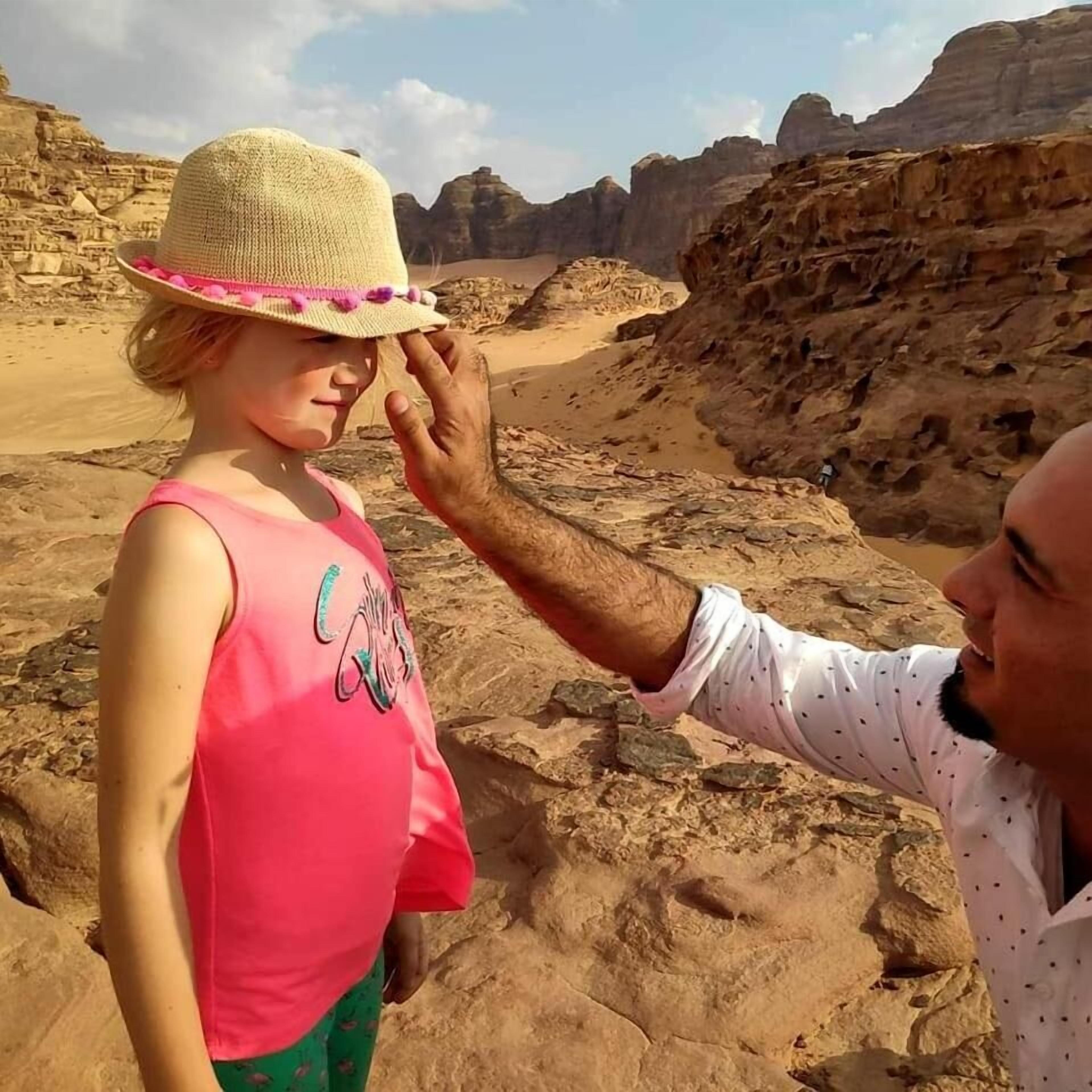 A person adjusting another person's hat in a rocky outdoor setting.