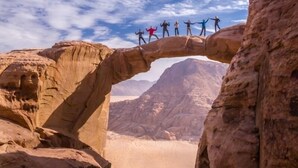 A natural rock formation with a group of people standing on top. - Oryx camp (Wadi Rum)