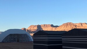 A desert landscape with a large geodesic dome and a striped tent. - Oryx camp (Wadi Rum)