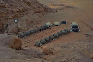 A desert landscape with a row of domed tents and rectangular buildings, likely accommodations, arranged in a linear fashion. - Oryx camp (Wadi Rum)