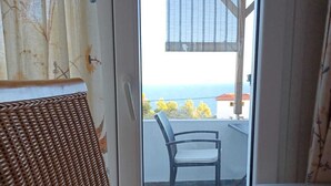 A room with a wicker chair, a small table, and a view of a balcony with a chair and a table. - Aloniro - Studio 1 (Alonnisos)