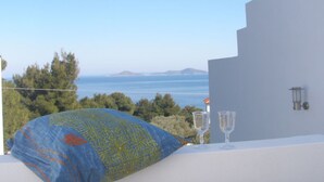 A balcony with a clear view of the sea and distant mountains, a blue patterned pillow, and two empty wine glasses on a white table. - Aloniro - Studio 1 (Alonnisos)