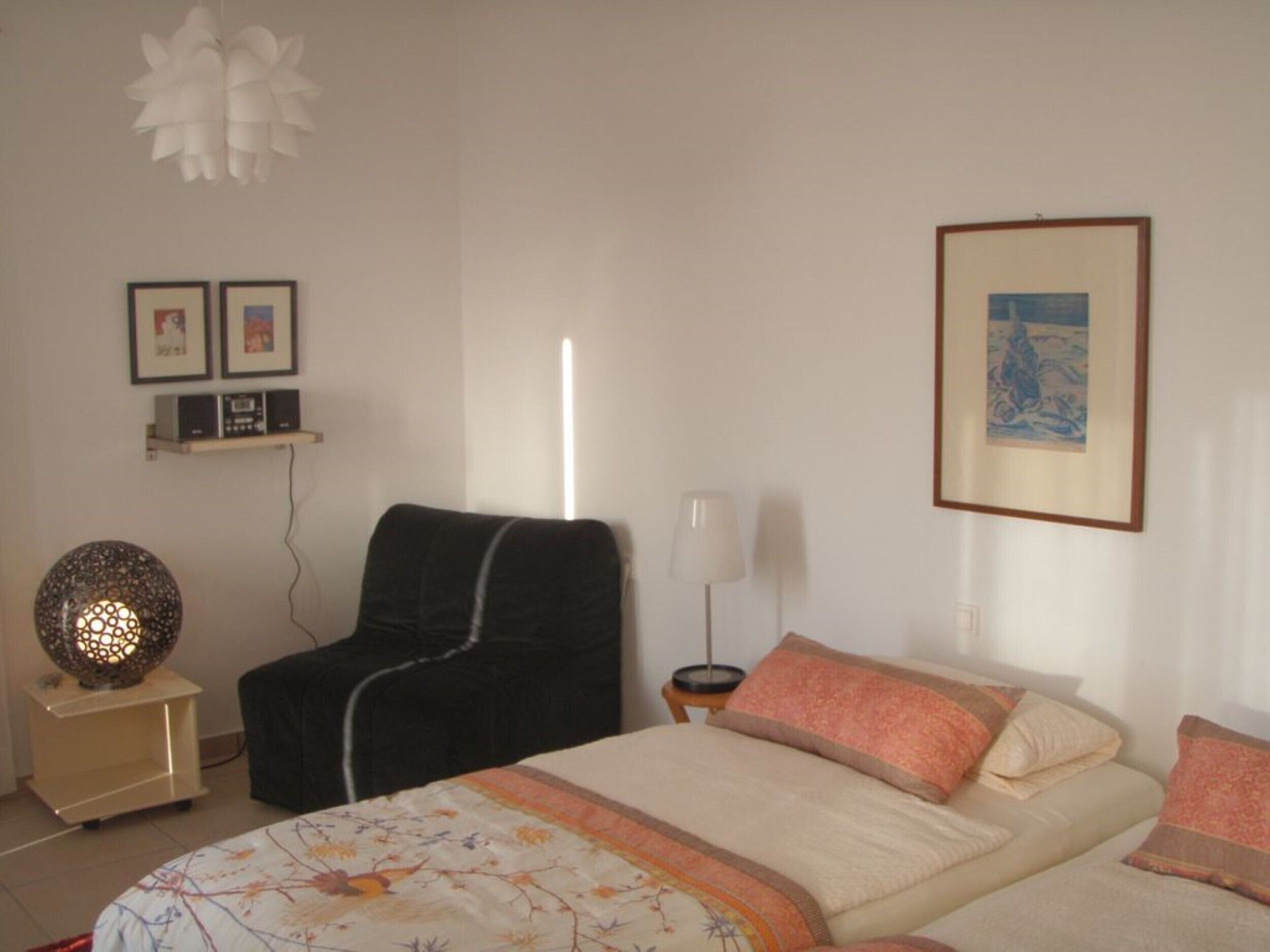 A bedroom with a bed, a chair, a bedside table, a lamp, and framed pictures on the wall.