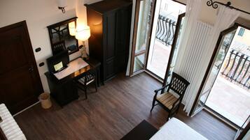 Ein Hotelzimmer mit Holzboden, einem Schreibtisch mit Lampe, einem Sessel, einem Bett und einem großen Fenster mit Blick nach draußen.