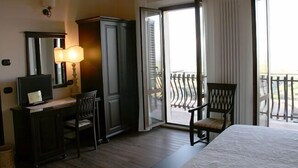 A hotel room with a bed, a desk with a computer, a chair, a wardrobe, and a balcony with a railing.