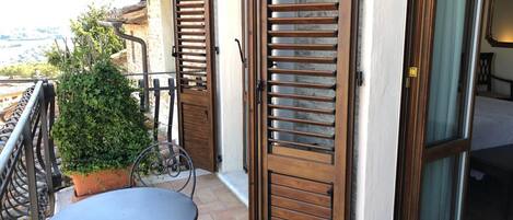 A balcony with a table and chairs, a potted plant, and a sliding glass door leading to a bedroom.