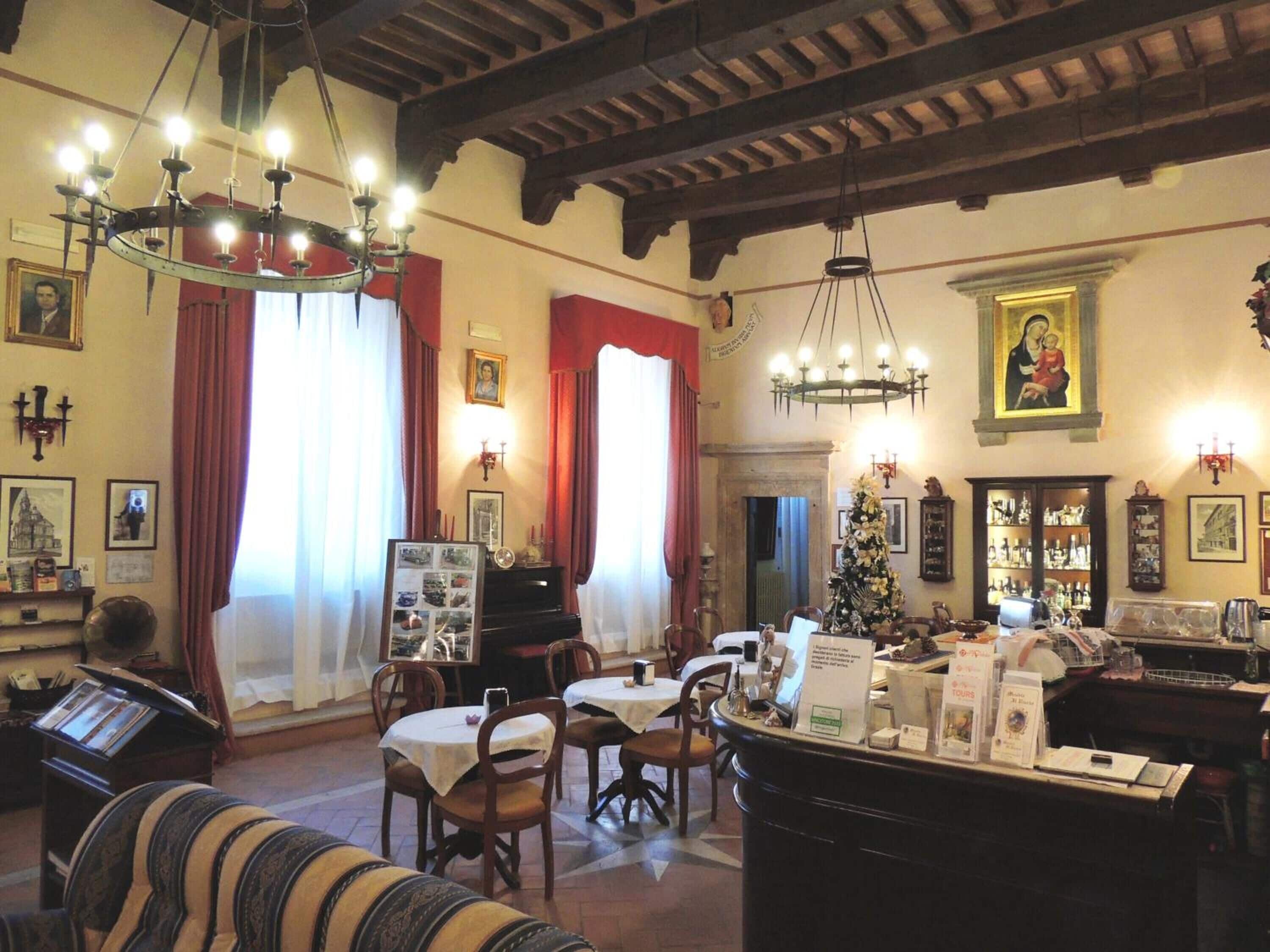 A traditional interior with exposed wooden beams, a piano, a Christmas tree, and a dining area with tables and chairs.