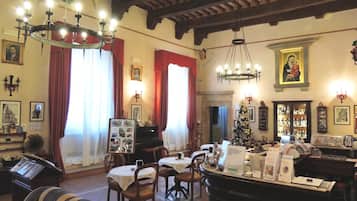 A traditional interior with exposed wooden beams, a piano, a Christmas tree, and a dining area with tables and chairs.