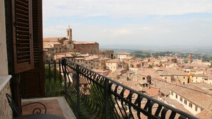 A balcony with a view of a historic town, featuring terracotta-roofed buildings and a prominent church tower.